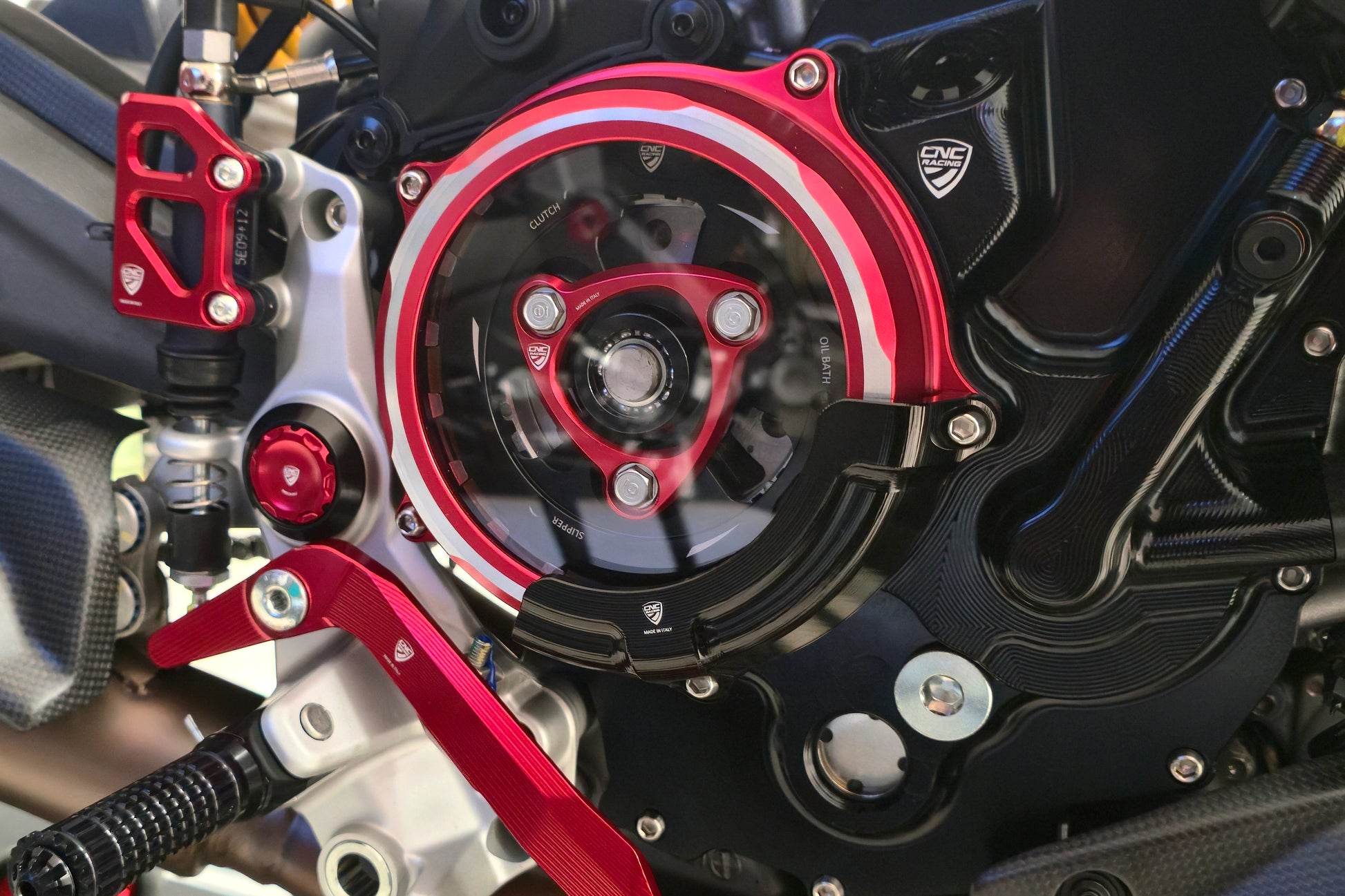 CNC Racing transparant koppelingsdeksel CA511BR met zwarte CAP03B beschermer gemonteerd op Ducati 890cc V2 – close-up van de complete montage met zicht op koppeling en voetsteun.